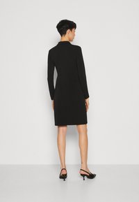 Svart långärmad klänning med en figurnära silhuett, slät textur och knälång fåll. Bärs med svarta slingback-klackar.