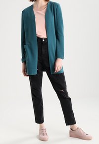 Tealowy sweter kardigan o fakturze, z otwartym przodem i bocznymi kieszeniami, w połączeniu z jasnoróżową bluzką, czarnymi, przetartymi dżinsami oraz jasnoróżowymi tenisówkami.