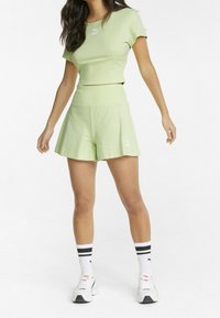 Hellgrünes Crop-Top und passende Shorts, gerippte Textur, Logo auf der Brust und am Bein, kombiniert mit weißen Socken mit schwarzen Streifen und Sportschuhen.