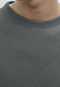 Grauer gerippter Pullover mit einem strukturierten Muster und klassischem Rundhalsausschnitt. Der Stoff wirkt weich mit dezenten Linien.