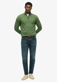Groene gebreide pullover met een kwartrits kraag, gecombineerd met blauwe denim jeans en beige sneakers. Gevarieerde stof, casual pasvorm ontwerp.