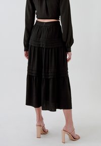 Gonna midi a balze nera con dettagli plissettati e chiusura con cerniera, realizzata in tessuto leggero. Indossata con sandali con tacco neutri.