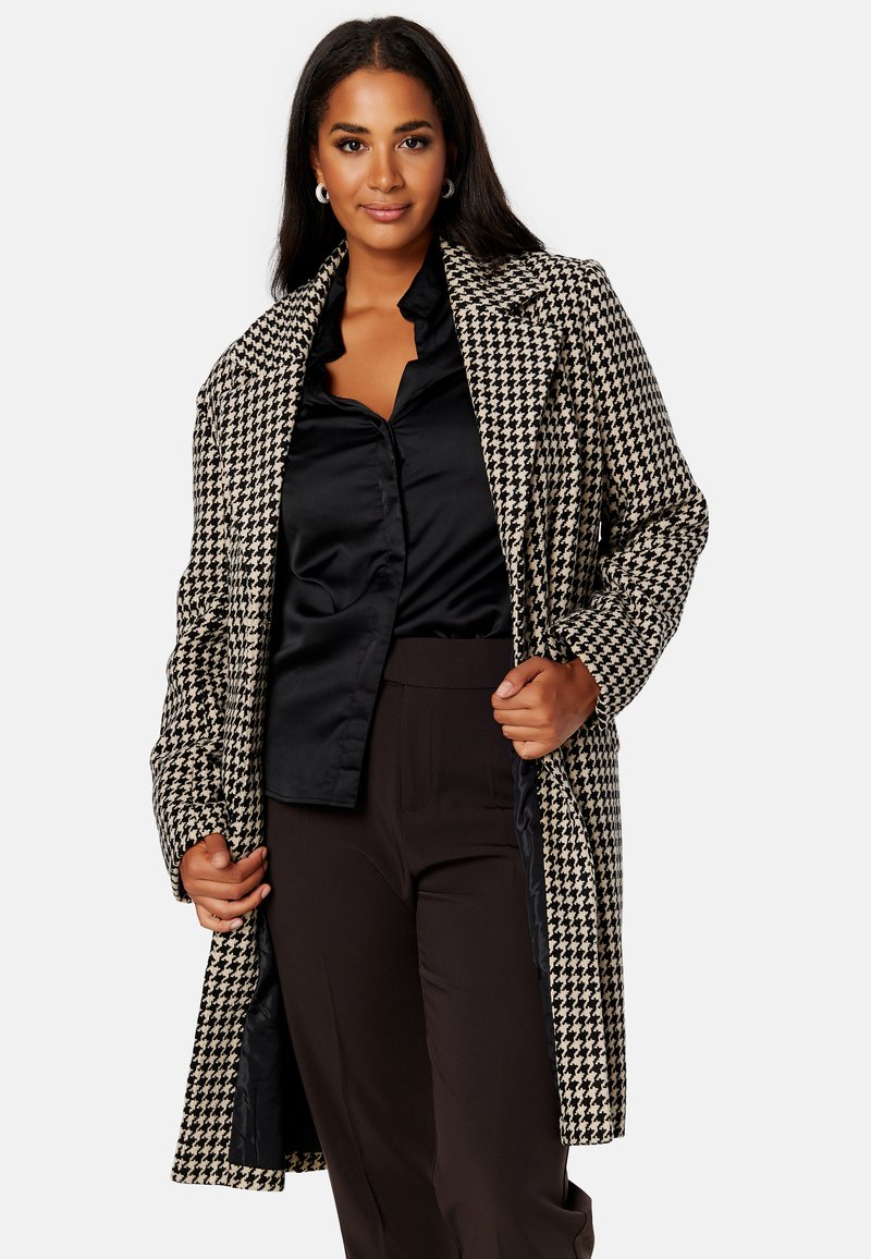 Cappotto a motivo pied-de-poule in bianco e nero con una vestibilità lunga e rilassata. Presenta rever a punta e tasche laterali. Fodera interna in raso.
