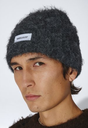 Ung mand iført en mørkegrå, fluffy hue med hvid label, en brun fluffy sweater og en lille hoop-ørering i venstre øre.