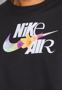 Svart sweatshirt med en stor "Nike Air"-logga som har färgglada blommönster, inklusive gula liljor och lila blommor, tryckt över bröstet.