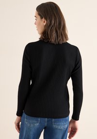 Zwarte geribbelde trui met lange mouwen en een ronde halslijn, gecombineerd met lichtblauwe jeans. De stof heeft een textuur met een verticaal patroon.