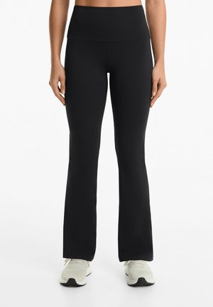 Leggings neri a palazzo con vita alta, realizzati in tessuto liscio ed elasticizzato. Abbinati a scarpe da ginnastica di colore chiaro.