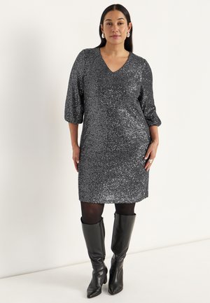 Silvrig paljettklänning med V-ringning och trekvartsärmar, med en rak skärning. Bärs med svarta knähöga stövlar. Slät textur.