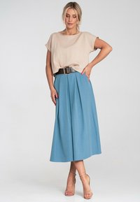Beżowa bluzka z krótkim rękawem o luźnym kroju w połączeniu z jasnoniebieską plisowaną spódnicą midi. Szeroki czarny pasek podkreśla talię.