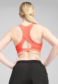 Red sports bra with a mesh back, featuring a racerback design and pink accents. Worn with black athletic shorts, showcasing a smooth texture.