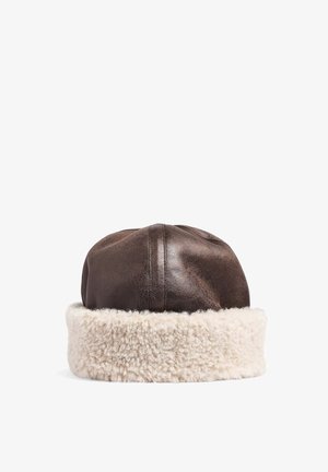 Chapeau en cuir marron avec une large bordure en peau lainée blanche duveteuse autour de la base, présenté sur un fond blanc.