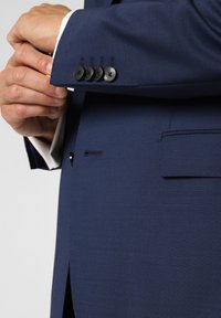 Giacca da abito blu scuro su misura con una texture liscia, dotata di quattro bottoni neri sul polsino e di una singola tasca sul petto.