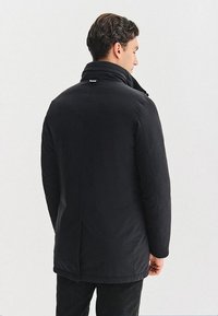 Czarna ocieplana kurtka z wysokim kołnierzem, zapięciem na zamek i rozcięciem z tyłu; gładka struktura bez widocznych wzorów czy detali sprzętowych.