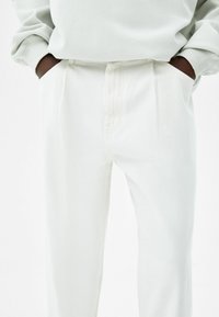 Pantalones plisados blancos hechos de una tela ligera, con bolsillos laterales y una textura suave, combinados con una sudadera de color claro.