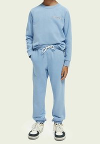 Felpa azzurra chiara con maniche raglan e logo ricamato, abbinata a pantaloni jogger coordinati con vita elasticizzata e polsini alle caviglie.