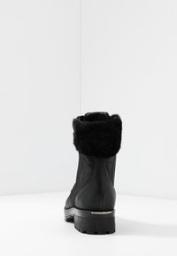  Sorte ankelstøvler med en tekstureret ruskindsfinish, der har en faux fur-krave og en robust sål. Lynlås på siden og logoaccent på hælen.