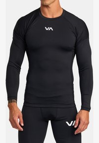 Zwart langslievend sportshirt gemaakt van rekbaar materiaal, met een aangesloten ontwerp en een wit logo op de borst en de onderzoom.
