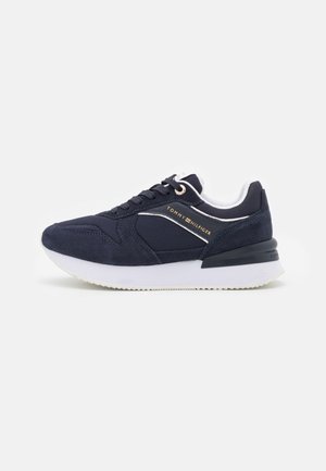Granatowy sneaker Tommy Hilfiger z białą podeszwą, sznurowanym przodem i logo po bokach, zaprojektowany do użytku codziennego.