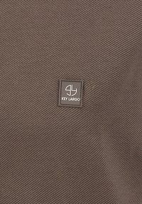 Tissu texturé brun avec un motif diagonal, comportant un petit badge carré sur lequel est inscrit "KEY LARGO" en lettres blanches.