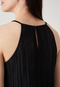 Czarny bezrękawnik z plisowanym wzorem, regulowanymi ramiączkami i małym wycięciem na plecach przy dekolcie. Gładka tekstura.
