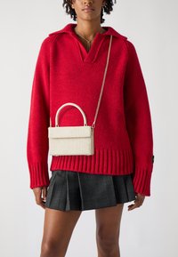 Rød strikket sweater med krave, parret med en hvid taske med krokodilleskindspræg, der har et håndtag og en kædesnor, sammen med en ternet nederdel.