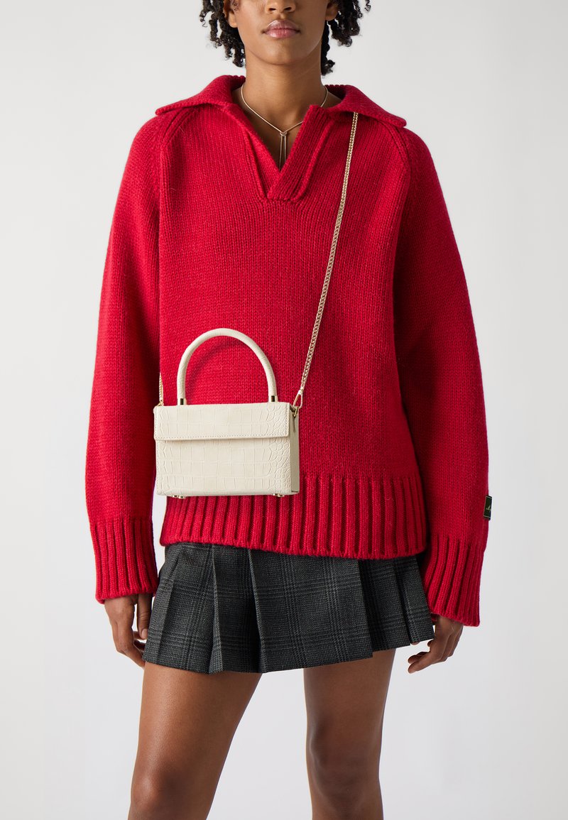 Rød strikket sweater med krave, parret med en hvid taske med krokodilleskindspræg, der har et håndtag og en kædesnor, sammen med en ternet nederdel.