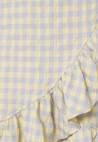 Žlutá a světle modrá kostkovaná látka s volánovým okrajem; měkká textura a tkaný vzor vytvářejí lehký, vzdušný vzhled.