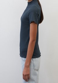 Námořnická modrá, krátký rukáv, top s vysokým límcem. Texturovaná látka s vodorovnými pruhy, mírné třepení na okrajích a přiléhavý střih.