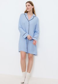 Abito camicia a maniche lunghe di colore azzurro chiaro con rifiniture nere, chiusura a bottoni e vestibilità comoda, realizzato in un tessuto morbido e liscio con una texture a coste.