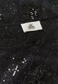 Sort pailletstof med et netoverlag, der har blomster mønstre. Et mærke er fastgjort, som læser "KBSS." Teksturen er skinnende og reflekterende.