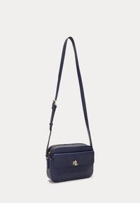 Tumši zila ādas plecu soma ar modernu dizainu, aprīkota ar priekšējo kabatu, zeltītu aparatūru un regulējamu siksnu. Gluda tekstūra.