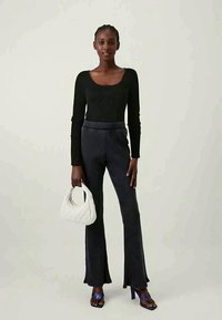 Melna garām piedurknēm tops, pieguļošs siluets; svītrainas, ar platām kājām pelēkas bikses; balta teksturēta rokassoma; zilas sandales ar siksniņām.