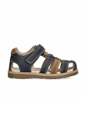 Sandalias con tiras de cuero azul marino y marrón, diseño abierto y cierre de velcro; acentuadas con costuras blancas y una suela beige.