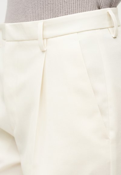 Kreminės spalvos kelnės su lygia priekinę dalimi, vienu klostėmis ir diržo kilpelėmis. Audinys yra lygios tekstūros, pritaikytas pagal figūrą.