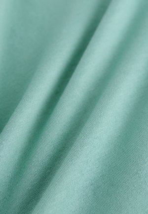 Jasnozielony materiał z gładką teksturą i subtelnymi delikatnymi wzorami tkania, tworzący łagodne fałdy na powierzchni.