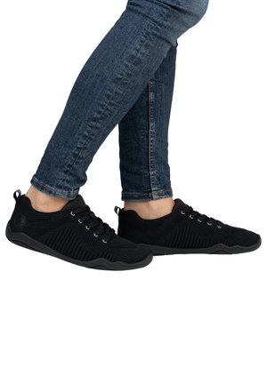 Black athletic shoes with a breathable knit upper, lace-up design, textured surface, and contrasting rubber sole, shown on a person’s feet.