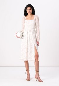 Rochie ușoară, imprimată floral, cu mâneci lungi, transparente, cu volane, un bust smockuit și o fanta laterală, într-o paletă de culori pastelate delicate.