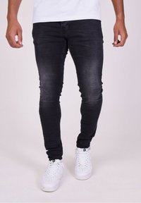Vaqueros ajustados negros con una textura desgastada, con una cintura de altura media y un ajuste ceñido, combinados con zapatillas deportivas blancas.