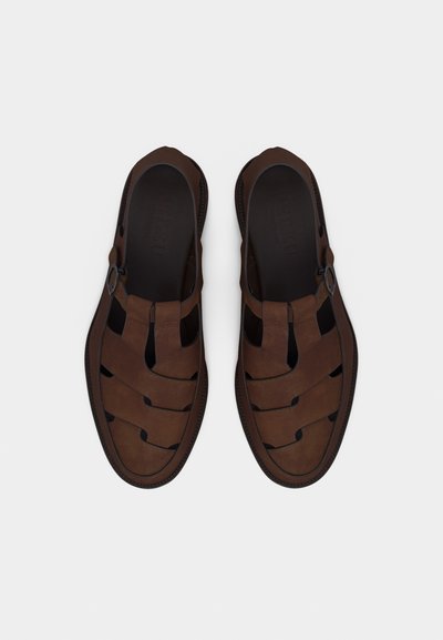 Ζευγάρι καφέ δερμάτινα ψαράδικα σανδάλια με ιμάντες με αγκράφα, ανοιχτές πλευρές και κλειστή μύτη, φωτογραφημένα από πάνω σε απλό φόντο.