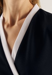 Primo piano del collo e della clavicola di una persona che indossa un indumento nero con un colletto bianco a forma di V.