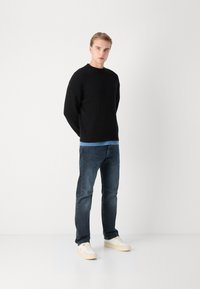 Czarny prążkowany sweter na jasnoniebieskiej koszuli, w połączeniu z ciemnymi wyblakłymi dżinsami i białymi trampkami. Prosty design, dopasowany krój, minimalne akcenty.