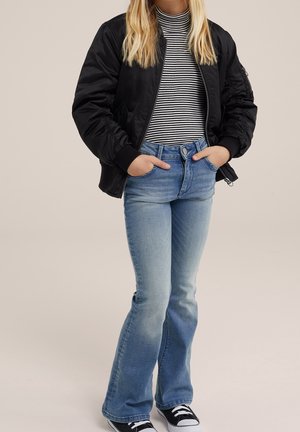 Black bomber jacket, striped long-sleeve shirt, light blue flared jeans, and black sneakers. Focus on casual urban fashion.