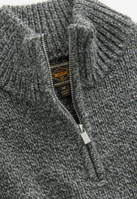 Grijs gebreide pullover met een hoge kraag en ritsluiting. Gelaagd stof met een gespikkeld patroon en een label dat maat en merk aangeeft.