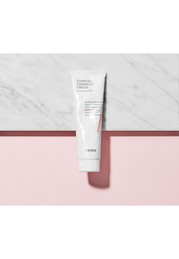 Tube blanc de "Comfort Ceramide Cream" de COSRX avec des accents roses, sur une surface en marbre, présentant un étiquetage clair et une texture lisse.