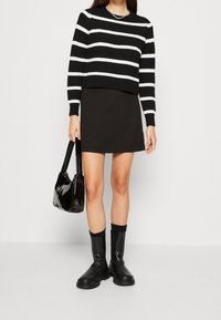 Pull en tricot rayé noir et blanc, mini jupe noire, sac à main noir brillant et bottes noires à semelle épaisse. Silhouette simple et moderne.