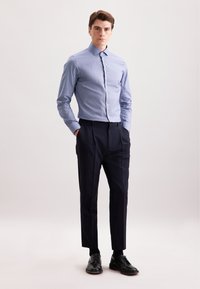 Camicia a righe blu chiaro con maniche lunghe, frontale con bottoni, abbinata a pantaloni a pieghe blu navy e scarpe stringate nere. Texture liscia.