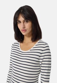 Maglietta a maniche lunghe a righe in crema con righe orizzontali blu navy. Presenta un'ampia scollatura e un tessuto morbido e testurizzato.