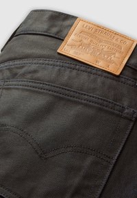 Achterzak van zwarte Levi's jeans met geborduurd ontwerp en tan leren Levi Strauss & Co. merklabel op de tailleband.