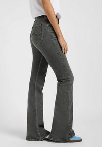Jean en denim gris évasés avec une taille mi-haute, coutures visibles et poches arrière. Le matériau a une texture légèrement décolorée.