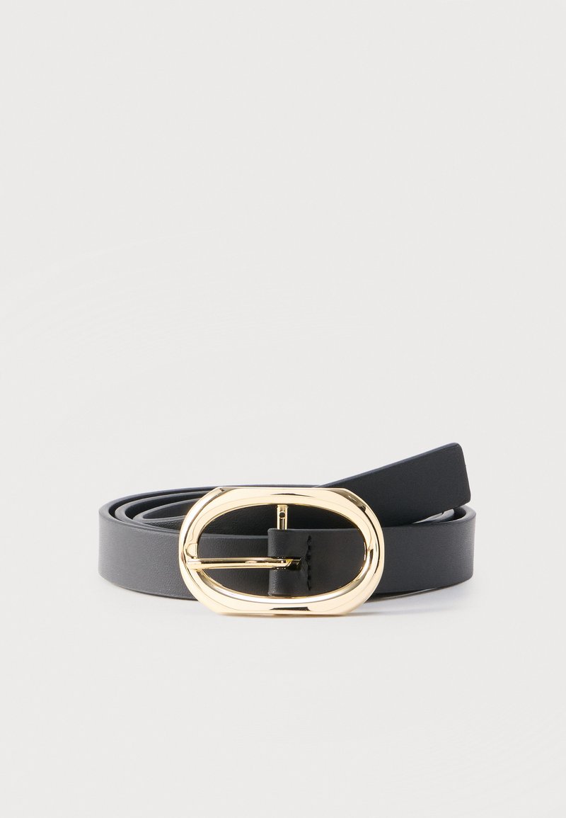 Μαύρη δερμάτινη ζώνη με λαμπερή χρυσή οβάλ αγκράφα, τυλιγμένη σε απλό ανοιχτό γκρι φόντο.